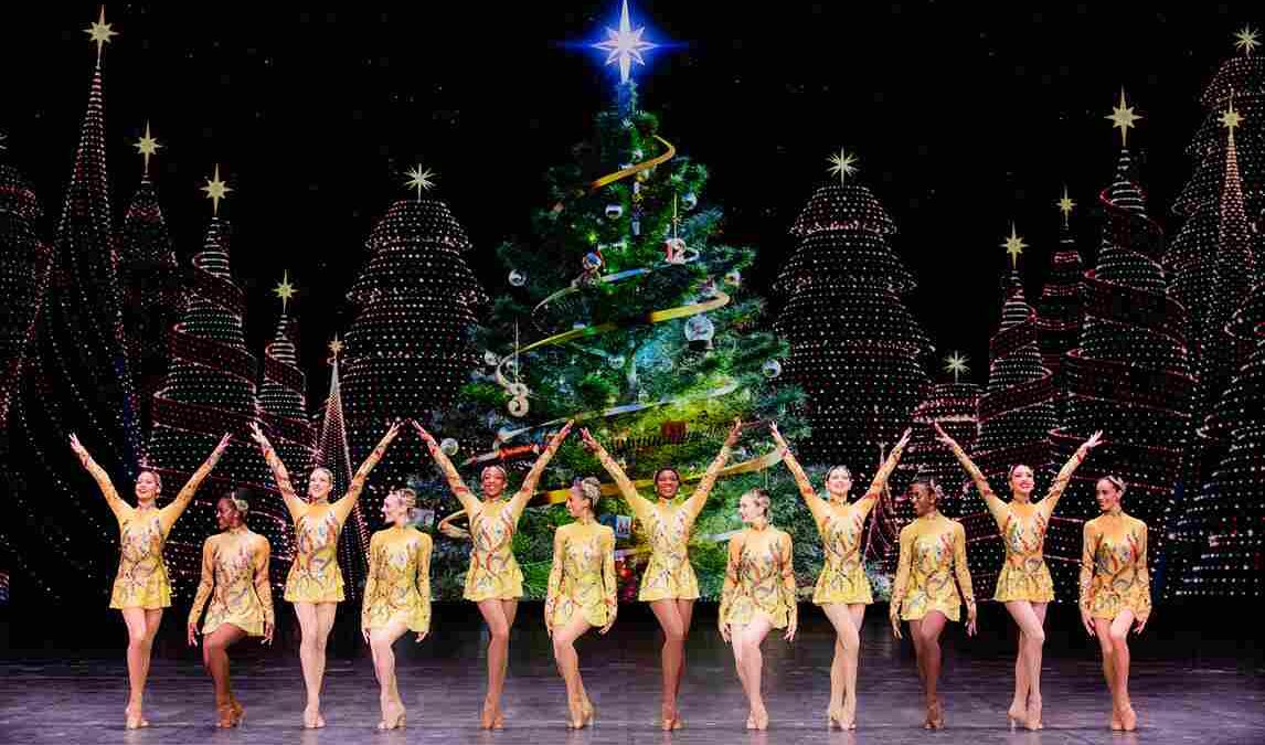 12 Rockettes on Stage in front of a Christmas tree